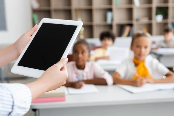 Vista parcial del profesor sosteniendo tableta digital con pantalla en blanco cerca de alumnos multiculturales - foto de stock