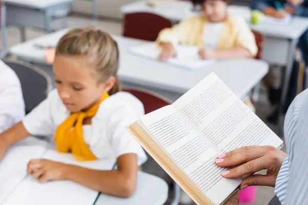 Vista ritagliata del libro di lettura insegnante vicino agli alunni in classe — Foto stock