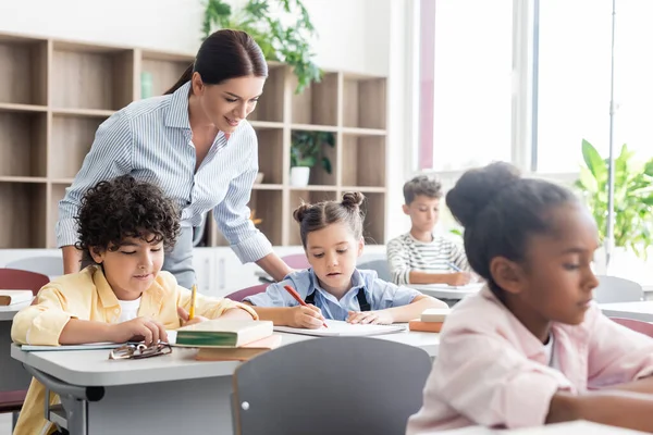 Focus selettivo dell'insegnante in piedi vicino agli alunni multietnici durante la lezione a scuola — Foto stock