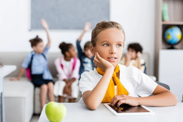 Selektiver Fokus der Schülerin, die in der Nähe von digitalem Tablet und Apfel auf dem Schreibtisch im Klassenzimmer wegschaut — Stockfoto