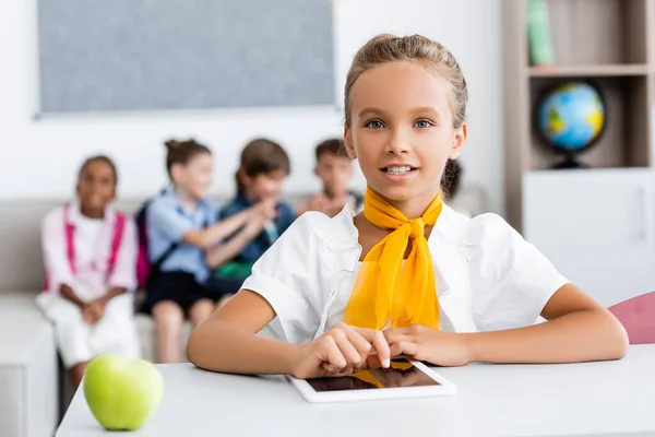 Селективный фокус школьницы с помощью цифрового планшета рядом с яблоком и мультикультурных одноклассников в классе — стоковое фото