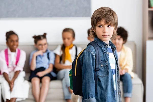 Выборочный фокус школьника с рюкзаком, смотрящего в сторону рядом с многонациональными друзьями в школе — стоковое фото