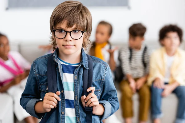 Selective focus of schoolboy in eyeglasses holding backpack in classroom — Stock Photo