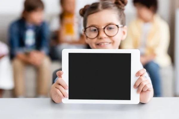 Selective focus of schoolgirl showing digital tablet with blank screen at desk — Stock Photo