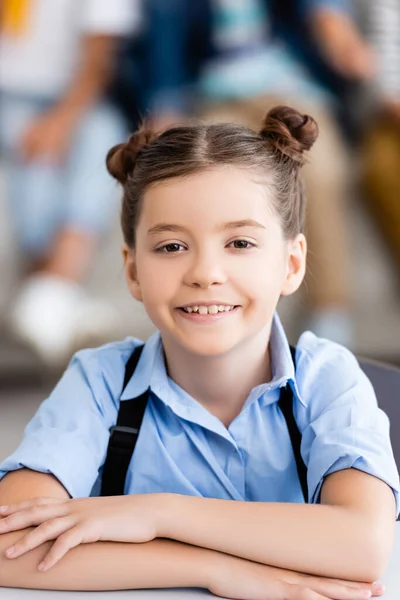 Selective focus of schoolgirl with backpack looking at camera at desk — Stock Photo