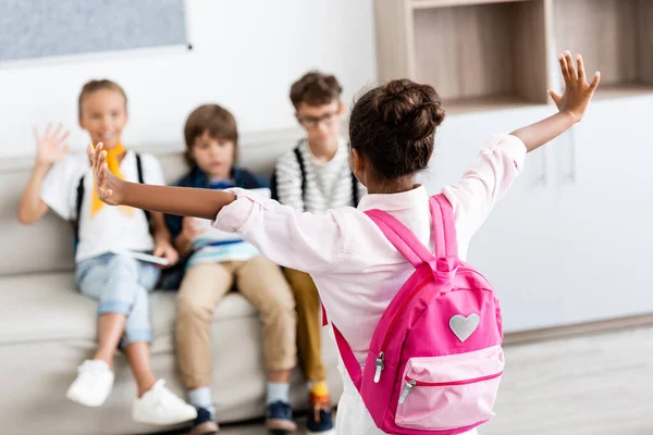 Concentration sélective de l'écolière afro-américaine avec sac à dos debout près des camarades de classe à l'école — Photo de stock