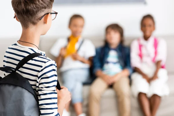 Selective focus of schoolboy with backpack standing near multiethnic friends in classroom — Stock Photo