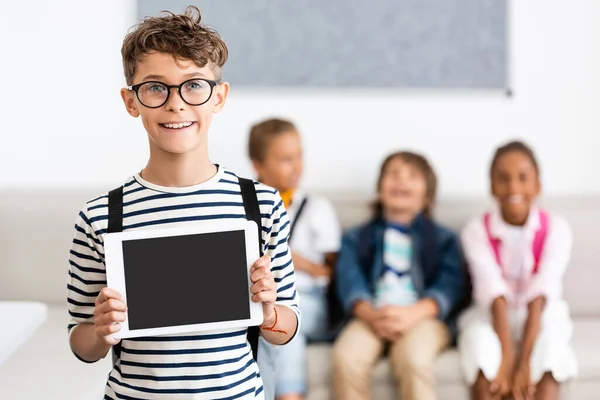 Selective focus of schoolboy in eyeglasses showing digital tablet with blank screen in classroom — Stock Photo