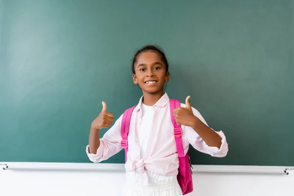 Afroamerikanische Schülerin zeigt Daumen nach oben in der Nähe von Kreidetafel im Klassenzimmer — Stockfoto