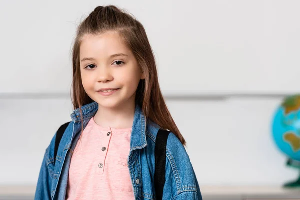 Schoolgirl with backpack looking at camera in classroom — Stock Photo