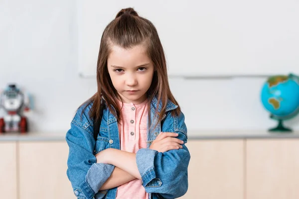 Confident schoolchild with crossed arms looking at camera in classroom — Stock Photo