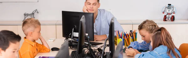 Panoramic shot of teacher looking at multiethnic schoolkids during lesson in stem school — Stock Photo