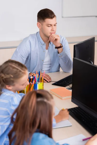 Foco seletivo do professor usando computador perto de alunas em sala de aula — Fotografia de Stock