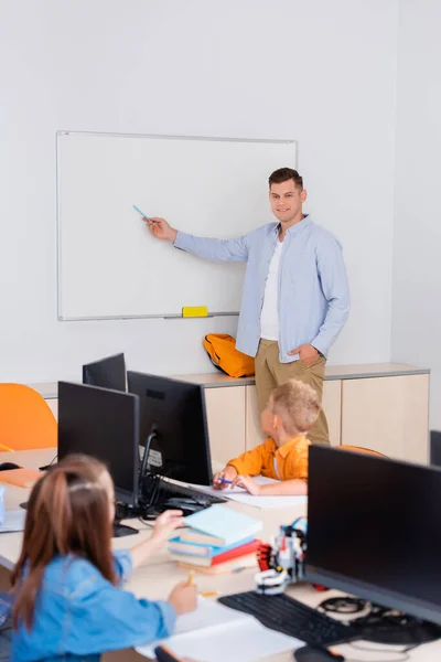 Foco seletivo do professor apontando para quadro branco perto de escolares na escola-tronco — Fotografia de Stock