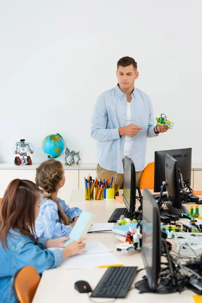 Selective focus of teacher pointing at robot near schoolgirls and computers in classroom — Stock Photo