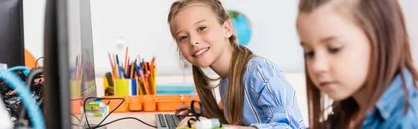 Panoramaaufnahme einer Schülerin, die in der Stammschule in die Kamera neben Freund und Computer blickt — Stockfoto
