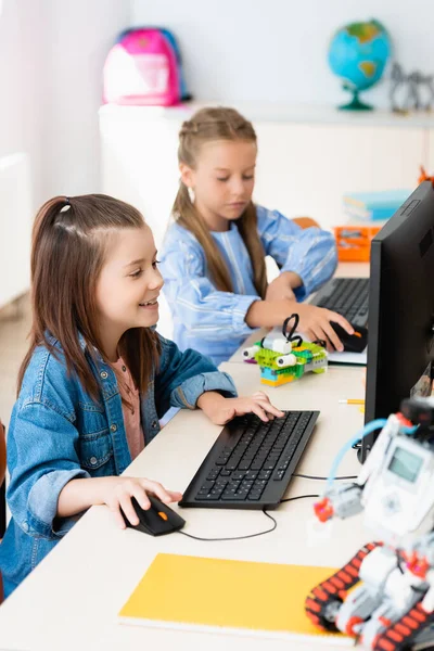 Foco seletivo de alunas usando computadores perto de robôs na escola-tronco — Fotografia de Stock