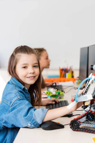 Selective focus of schoolgirl looking at camera near robot and computers in stem school — Stock Photo