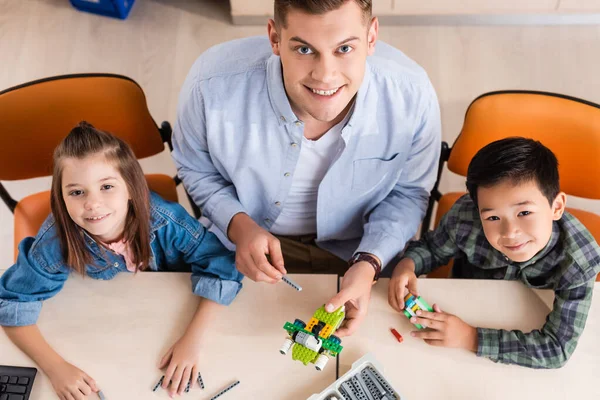 Overhead view of teacher and multiethnic pupils looking at camera while modeling robot in classroom — Stock Photo