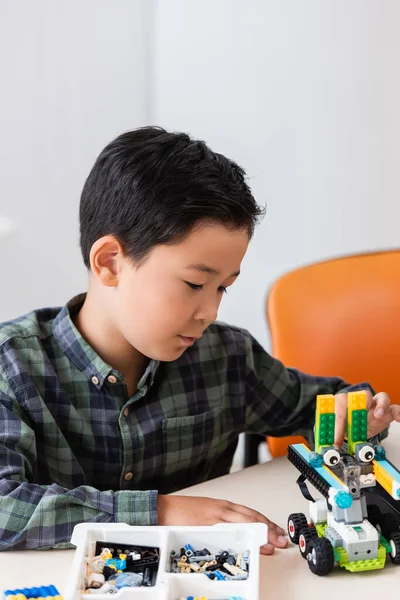 Selective focus of asian schoolboy looking at robot near building blocks on table in stem school — Stock Photo