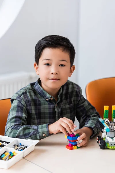 Selective focus of asian schoolboy holding building blocks while modeling robot in stem school — Stock Photo