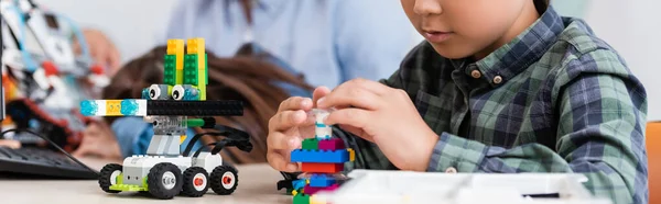 Panoramic crop of schoolboy with building blocks modeling robot in stem school — Stock Photo
