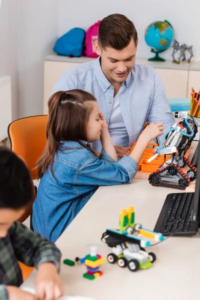 Selective focus of teacher and schoolgirl modeling robot near computer in stem school — Stock Photo