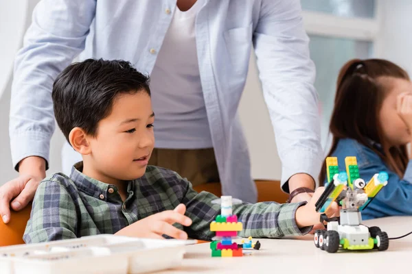 Enfoque selectivo de profesor de pie cerca asiático escolar modelado robot en tallo escuela - foto de stock