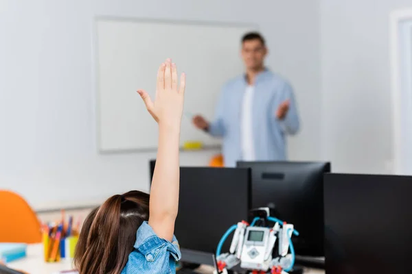 Selective focus of schoolgirl with raised hand near robot and computers in stem school — Stock Photo