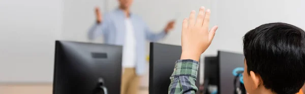 Horizontal cosecha de asiático escolar con levantado mano sentado cerca de computadoras en tallo escuela - foto de stock