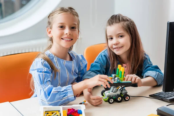 Selective focus of classmates holding robot near building blocks and computer on table — Stock Photo