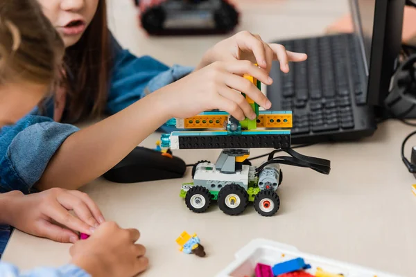 Selective focus of schoolgirls modeling robot from building blocks near computer in classroom — Stock Photo