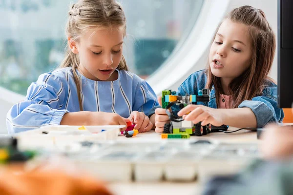 Selective focus of schoolgirl constructing robot near friend in stem school — Stock Photo