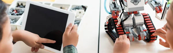 Encabezado del sitio web de escolares multiétnicos que utilizan tableta digital mientras programan robot en la escuela madre - foto de stock
