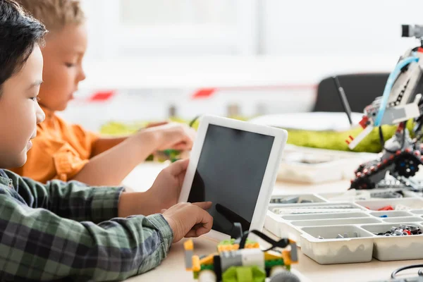 Selektiver Fokus asiatischer Schüler mit digitalem Tablet in der Nähe von Freunden und Robotern auf dem Tisch in der Schule — Stockfoto