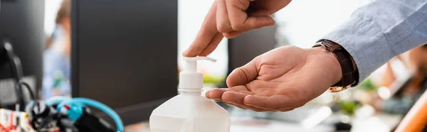 Panoramic crop of teacher using hand sanitizer in classroom — Stock Photo