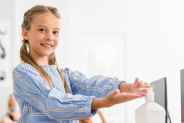 Concentration sélective de l'écolière regardant la caméra tout en utilisant un désinfectant pour les mains en classe — Photo de stock