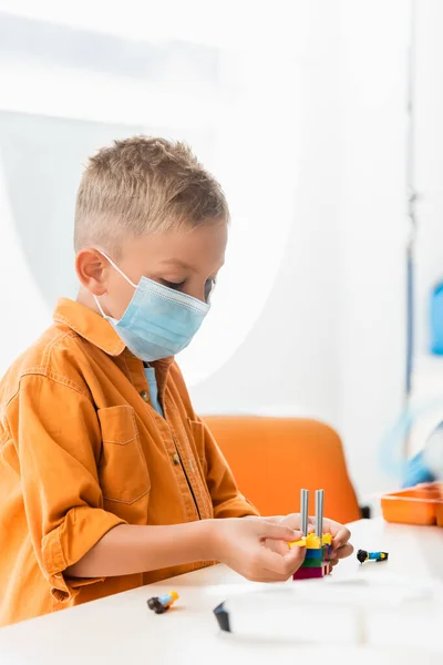 Selective focus of schoolboy in medical mask modeling robot with building blocks in stem school — Stock Photo