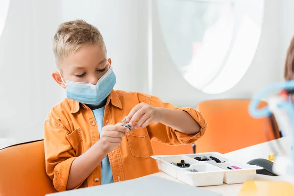 Selective focus of schoolboy in medical mask constructing robot in stem school — Stock Photo