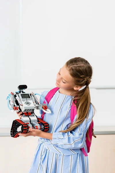 Schoolgirl with backpack holding robot in classroom of stem school — Stock Photo