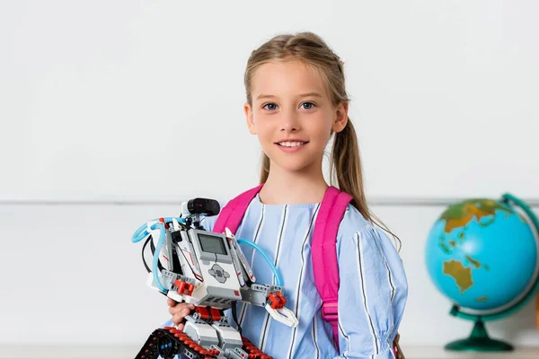 Schoolgirl holding robot and looking at camera in classroom — Stock Photo