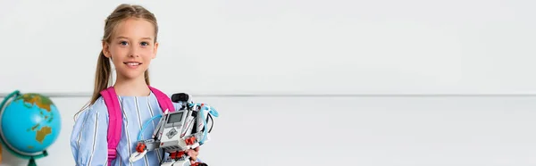 Panoramic crop of schoolchild holding robot and looking at camera in classroom — Stock Photo