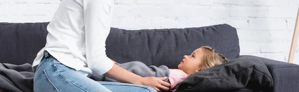 Cultura horizontal da mulher sentada ao lado da filha doente no sofá em casa — Fotografia de Stock