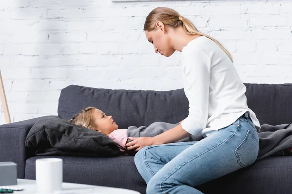 Selektive Berührung von Frau mit krankem Kind nahe Tasse auf Couchtisch zu Hause — Stockfoto