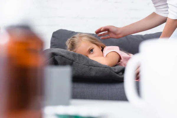 Selective focus of sick child looking at camera near mother on couch — Stock Photo