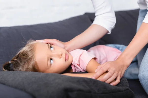 Enfoque selectivo del niño enfermo mirando a la madre mientras está acostado en el sofá - foto de stock