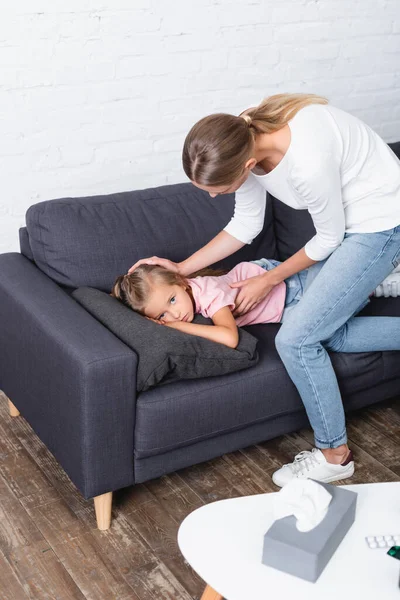 Foco seletivo da mulher acariciando a filha perto de guardanapos e pílulas na mesa de café em casa — Fotografia de Stock