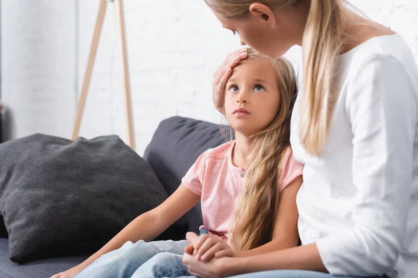 Selective focus of woman touching head of ill daughter at home — Stock Photo