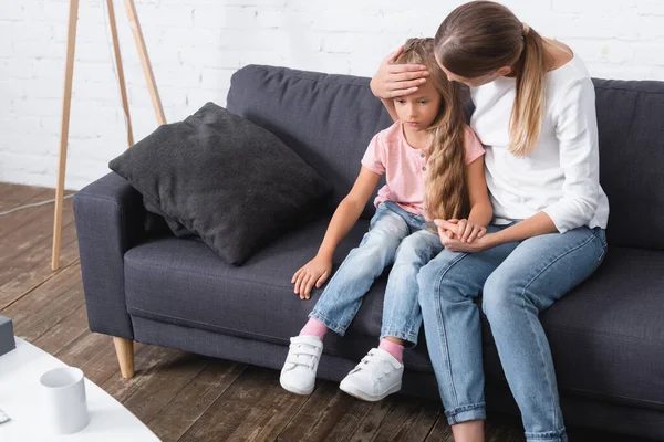 Selective focus of woman touching forehead of daughter on sofa — Stock Photo