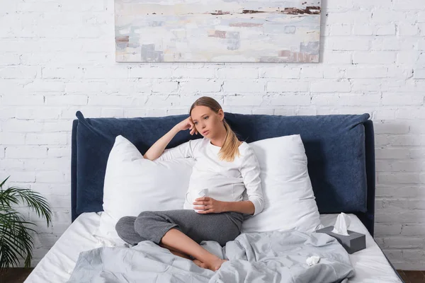 Selective focus of pregnant woman holding cup near napkins on bed — Stock Photo